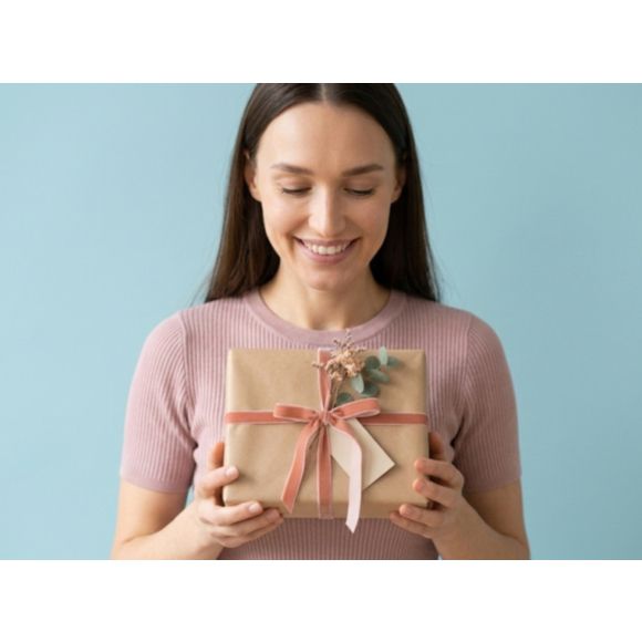 Uśmiechnięta kobieta z podarunkiem. Jaki prezent na Dzień Kobiet wybrać? Zestaw kosmetyków tołpa.® dla żony, mamy lub siostry.