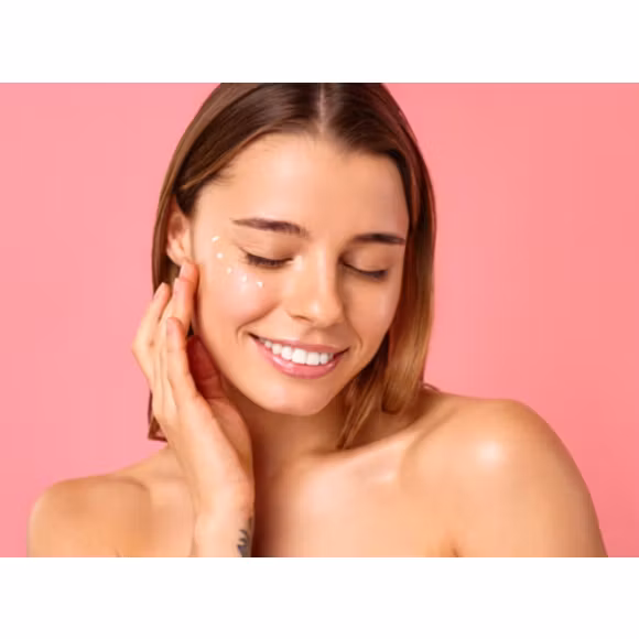 Uśmiechnięta kobieta z zamkniętymi oczami dotykająca dłonią twarzy na której ma kropki z kremu - tytułowa