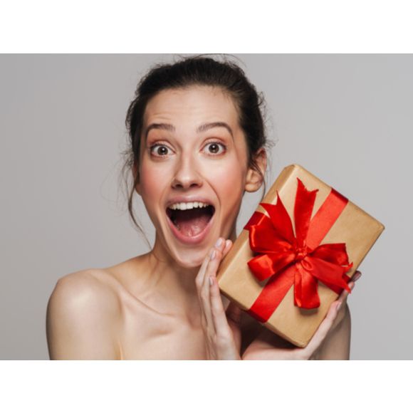 Alt: Zdziwiona kobieta trzymająca w rękach prezent na święta - zdjęcie