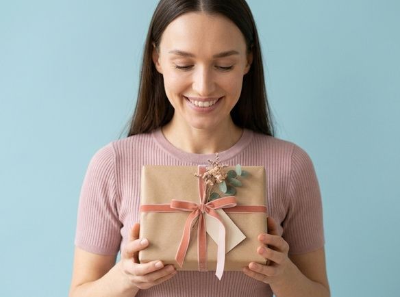 Uśmiechnięta kobieta z podarunkiem. Jaki prezent na Dzień Kobiet wybrać? Zestaw kosmetyków tołpa.® dla żony, mamy lub siostry.