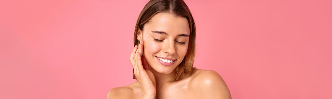 Uśmiechnięta kobieta z zamkniętymi oczami dotykająca dłonią twarzy na której ma kropki z kremu - tytułowa