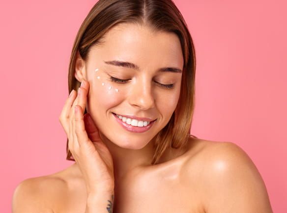 Uśmiechnięta kobieta z zamkniętymi oczami dotykająca dłonią twarzy na której ma kropki z kremu - tytułowa