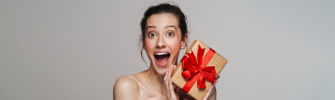 Alt: Zdziwiona kobieta trzymająca w rękach prezent na święta - zdjęcie