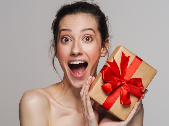 Alt: Zdziwiona kobieta trzymająca w rękach prezent na święta - zdjęcie