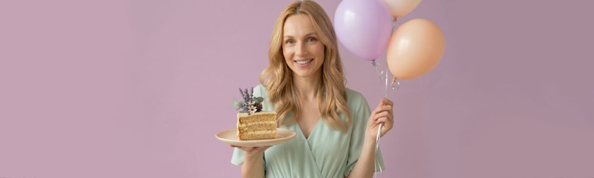 Uśmiechnięta kobieta o jasnych włosach trzymająca w dłoni kawałek tortu i balony - odkryj najlepsze naturalne kosmetyki tołpa.®z okazji naszych urodzin.